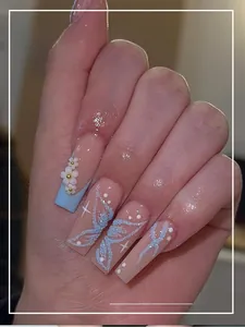 Détail macro de faux ongles longs avec fleurs 3D perles et motifs papillon bleu