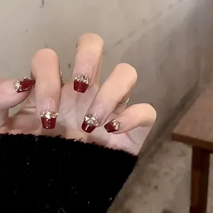 Detail view of burgundy handmade press-on nails with champagne glitter and gold foil accents