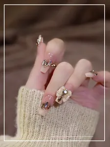 Detail of nude press-on nails featuring sparkling rhinestones and 3D white bow tie accents