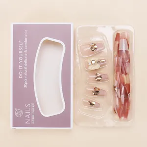 Close-up of champagne gold press-on nails with bow charms and glitter in display box
