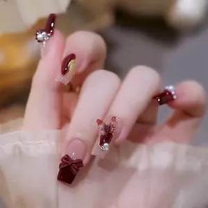 Detail of red press-on nails featuring 3D bows, pearls, and a metallic rabbit motif