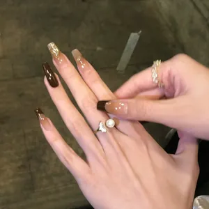 Detail of long coffin press-on nails with brown gradient, gold foil and pearl rings