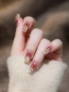Makroaufnahme von roten Ombré-Kunstnägeln mit goldenem Glitzer und Strass-Akzenten