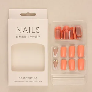 Short orange press-on nails with white gradient and rhinestones in professional box