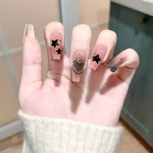 Macro detail of gradient pink coffin press-on nails with black stars and 3D heart charm