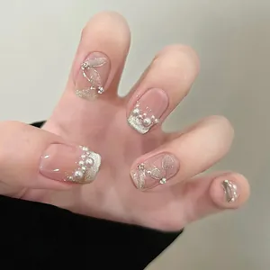 Detailed shot of French tip press-on nails with pearls and rhinestone leaf design