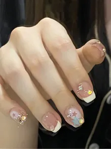 Nahaufnahme von rosa Kunstnägeln mit French Tips, goldenen Schleifen und Strasssteinen