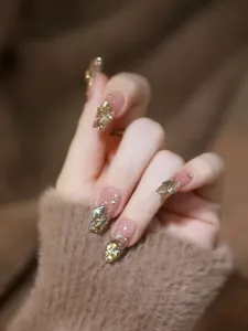 Nahaufnahme von nude-rosa Kunstnägeln mit goldenen Strasssteinen und Glitzereffekt