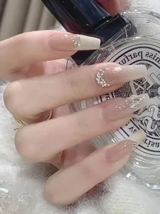Nahaufnahme von Nude-Gradient-Nägeln mit goldenen Schleifen und Herz-Strass-Dekor