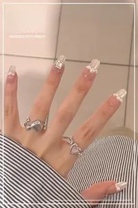 Detail of milky white aurora press-on nails with elegant pearls and silver rings