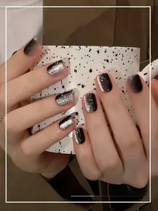 Detail of black gradient cat eye press-on nails with silver glitter on hands holding a cup