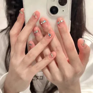 Faux ongles rose transparent avec strass colorés sur une main pour un look tendance