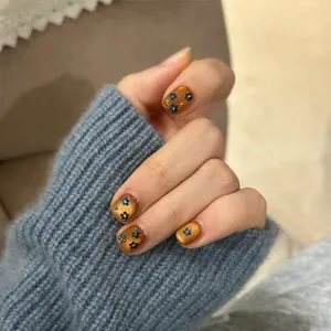 Dettaglio di unghie cat-eye marrone dorato con motivi floreali blu dipinti a mano