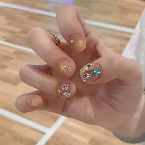 Pink press-on nails with yellow stars and colorful 3D rhinestones on hand model