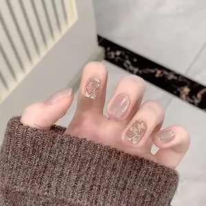 Detail of short press-on nails with nude pink finish, gold foil accents and glitter details