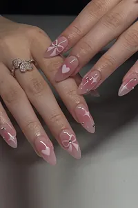 Close-up of pink gradient press-on nails with white hearts, bows, and 3D silver beads