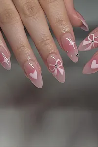 Close-up of pink press-on nails with white heart, bow, and star hand-painted designs