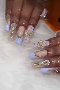 Gros plan sur de longs faux ongles avec papillon doré 3D, strass et pétales violets chics