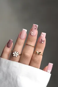 Détail d'ongles roses pailletés avec motifs marguerites et bagues dorées