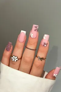 Détail d'ongles roses pailletés avec French tips blanches et motifs floraux peints à main