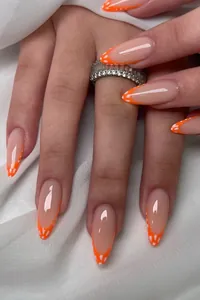 Details von langen Mandel-Kunstnägeln mit orangefarbenen Spitzen und weißen Punkten
