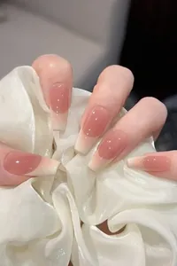 Close-up of long coffin French press-on nails with nude pink gradient and glossy finish