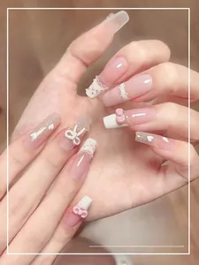 Detail of press-on nails with pink bows, pearls, and glitter on long coffin shape