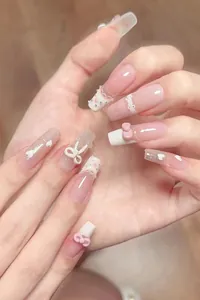 Detail of pink and white press-on nails with 3D bows, pearls, and lace texture patterns