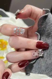 Detail of red cat-eye press-on nails with silver glitter, polka dots and bow rhinestones