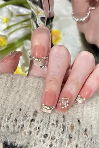Detail of pink cat eye press-on nails with French gold tips, pearls and rhinestones
