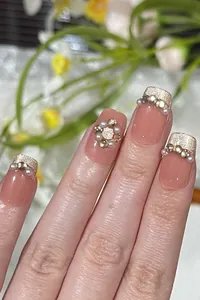 Detail of pink French press-on nails with pearls, gold glitter, and luxury rhinestones