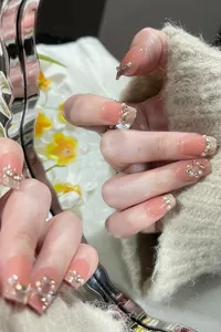 Close-up of pink press-on nails with pearl accents and golden beads in soft lighting