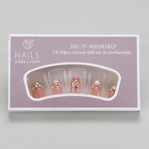 Detail of nude pink press-on nails set with glitter tips and pearl charms in packaging