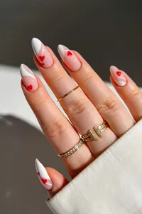 Close-up of almond-shaped fake nails with white wave patterns and red heart art designs