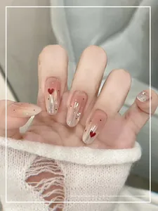 Detail of gradient pink press-on nails with red heart patterns and sparkling rhinestones