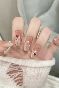 Close-up of almond-shaped press-on nails with pink gradient, red hearts and crystals