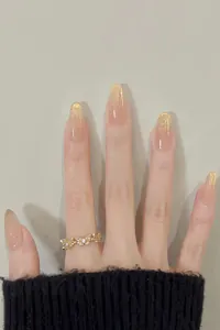 Macro view of long almond press-on nails with gold glitter gradient on nude pink base