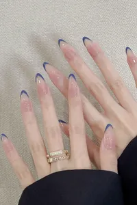 Detail of almond-shaped press-on nails with nude base and deep blue French tips
