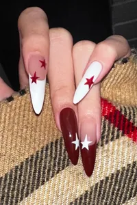Detail of almond-shaped press-on nails with red and white star motifs on fabric