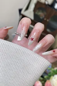 Close-up of almond nails featuring silver glitter gradient and red star patterns