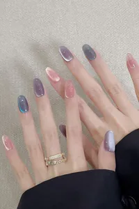 Detailed view of almond cat-eye nails in violet and pink shimmer with golden ring accessories