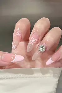 Macro di unghie a mandorla rosa con punte French, strass e decorazioni a fiocco eleganti