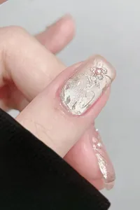 Gros plan sur des faux ongles œil-de-chat rose nude avec fleurs 3D et détails en perles