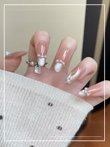 Détail de faux ongles nude avec pointes œil de chat blanches et mini perles fines