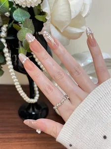 Détail de faux ongles ovales longs avec dégradé nude et décorations de perles blanches