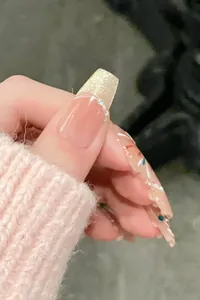 Macro shot of nude pink press-on nails with gold glitter, pearls, and white line details