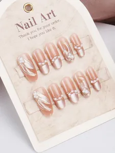 Détail de faux ongles œil-de-chat rose nude avec perles blanches et motifs dorés en relief