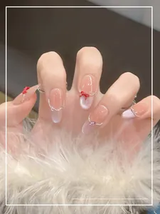 Detail of nude cat-eye press-on nails with red bows and silver bead chains on model's hand