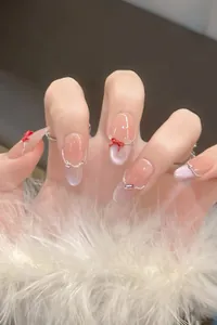 Macro detail of nude cat eye press-on nails with red bow and rhinestone accents