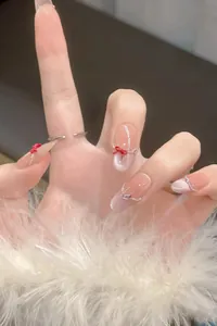 Detail of nude cat-eye press-on nails with 3D red bows and delicate silver chains
